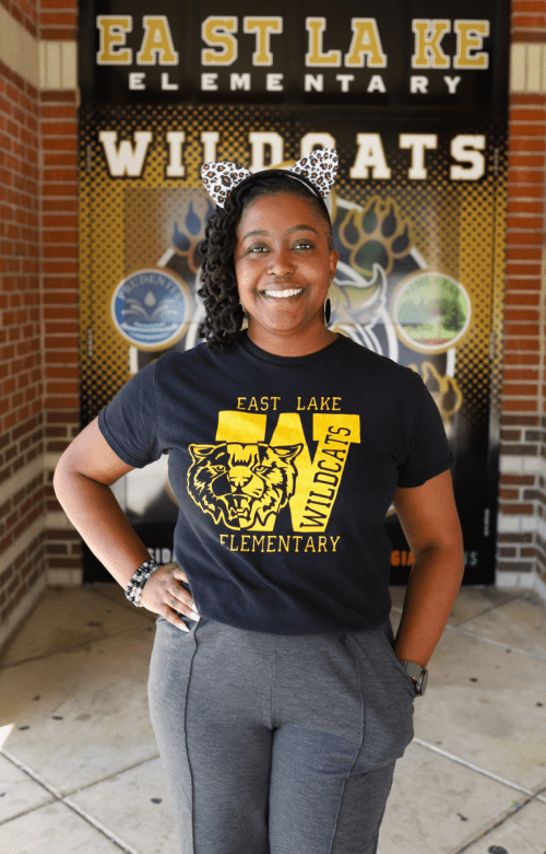 NEWSROOM COVER - Dr. Jasmine Farrow Dr. Jasmine Farrow Principal at east lake elementary in front of school with ears on in east lake shirt