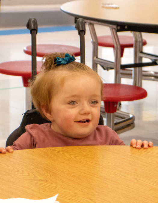 child in wheelchair sitting at lunchroom table